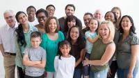 A multi-ethnic group of multiple generations are standing together for a family reunion.